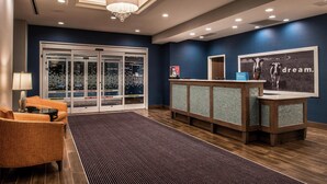 A hotel reception area with a modern design, featuring a reception desk, seating area, and a large glass door entrance.