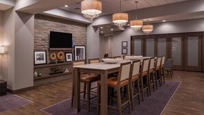 A dining area with a long table, chairs, and a television mounted on a stone wall.
