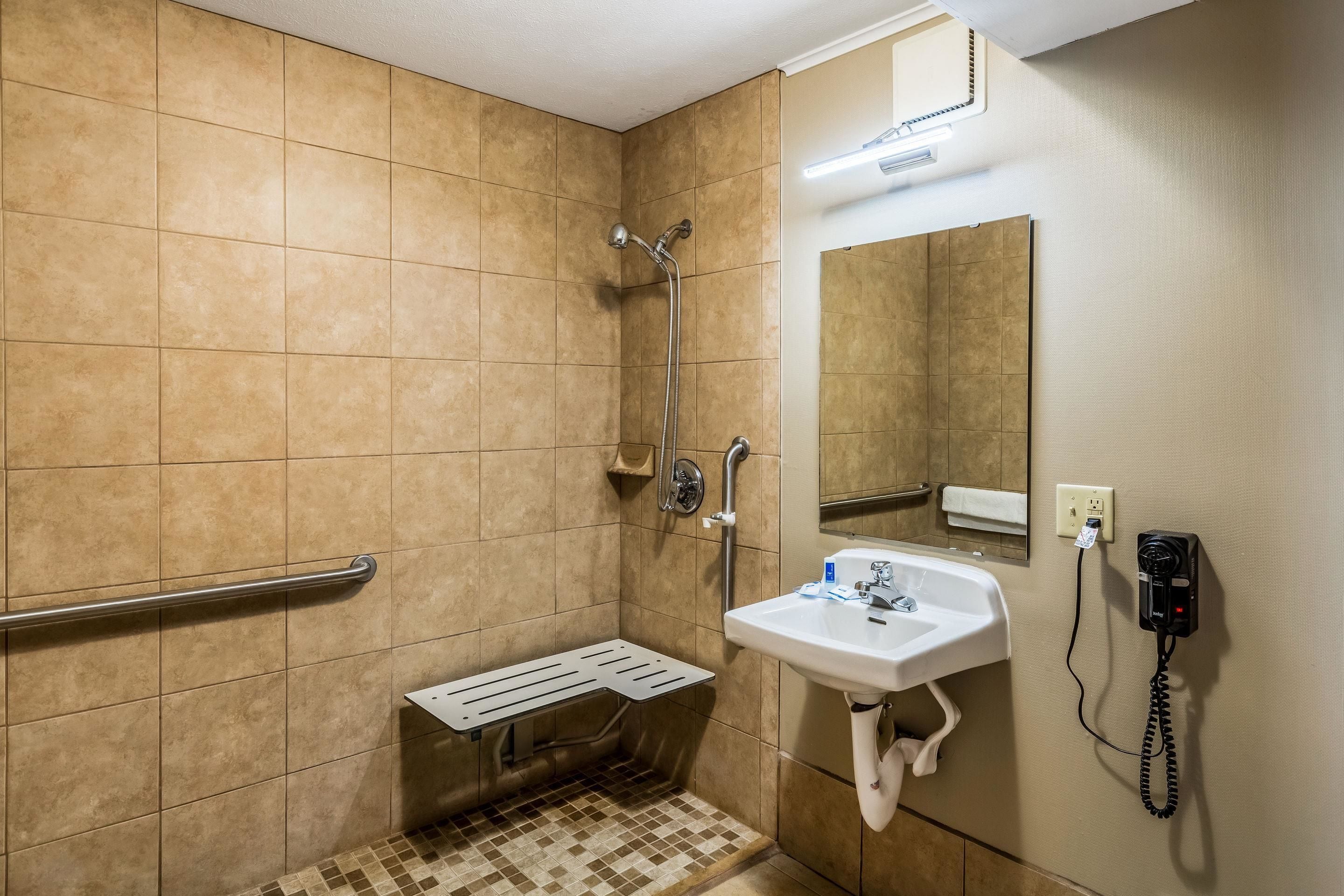 A bathroom with a shower, a sink, a hand dryer, and a telephone.