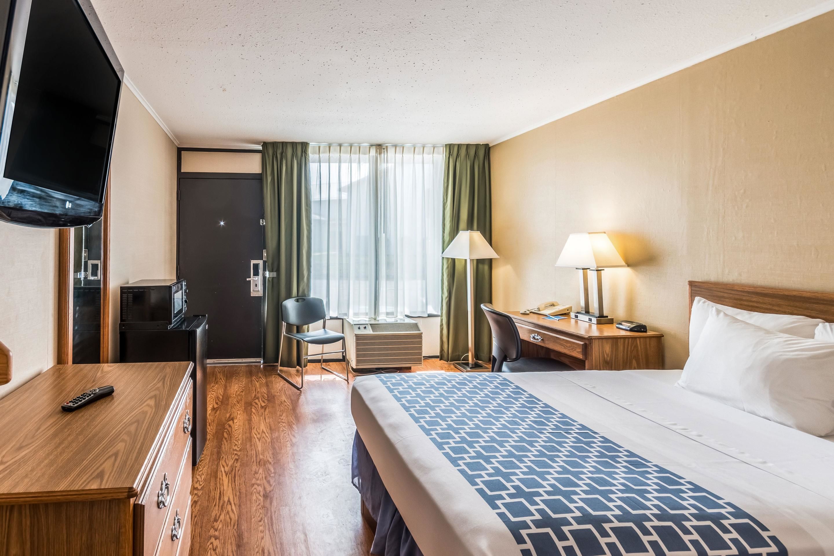 A hotel room with a bed, desk, chair, TV, and a microwave.