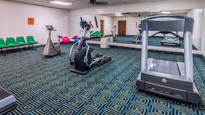 A gym with exercise equipment, green chairs, and a mirrored wall. - Smart Extended Stay (Beckley)