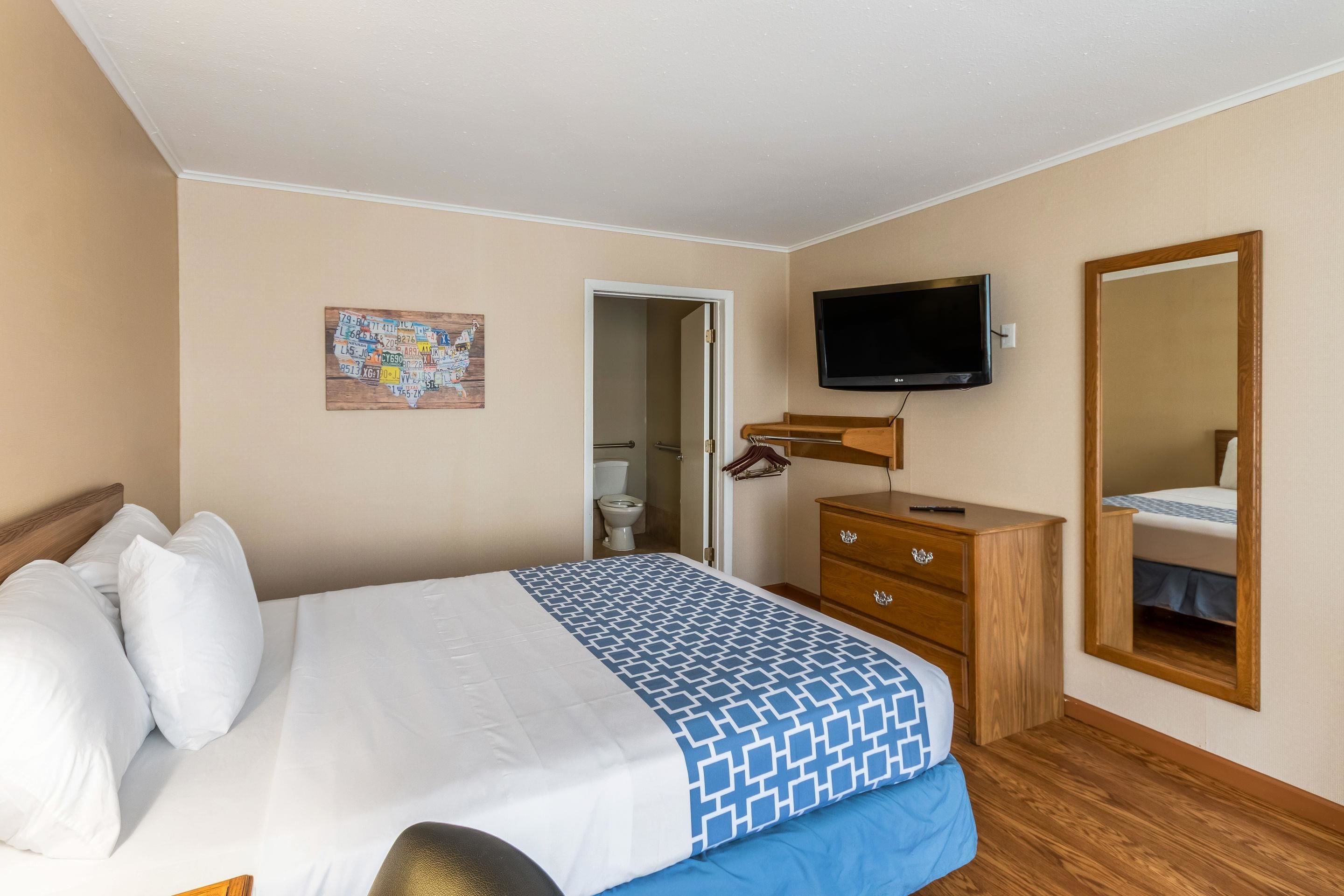 A hotel room with a bed, a dresser, a television, a mirror, and a map on the wall.