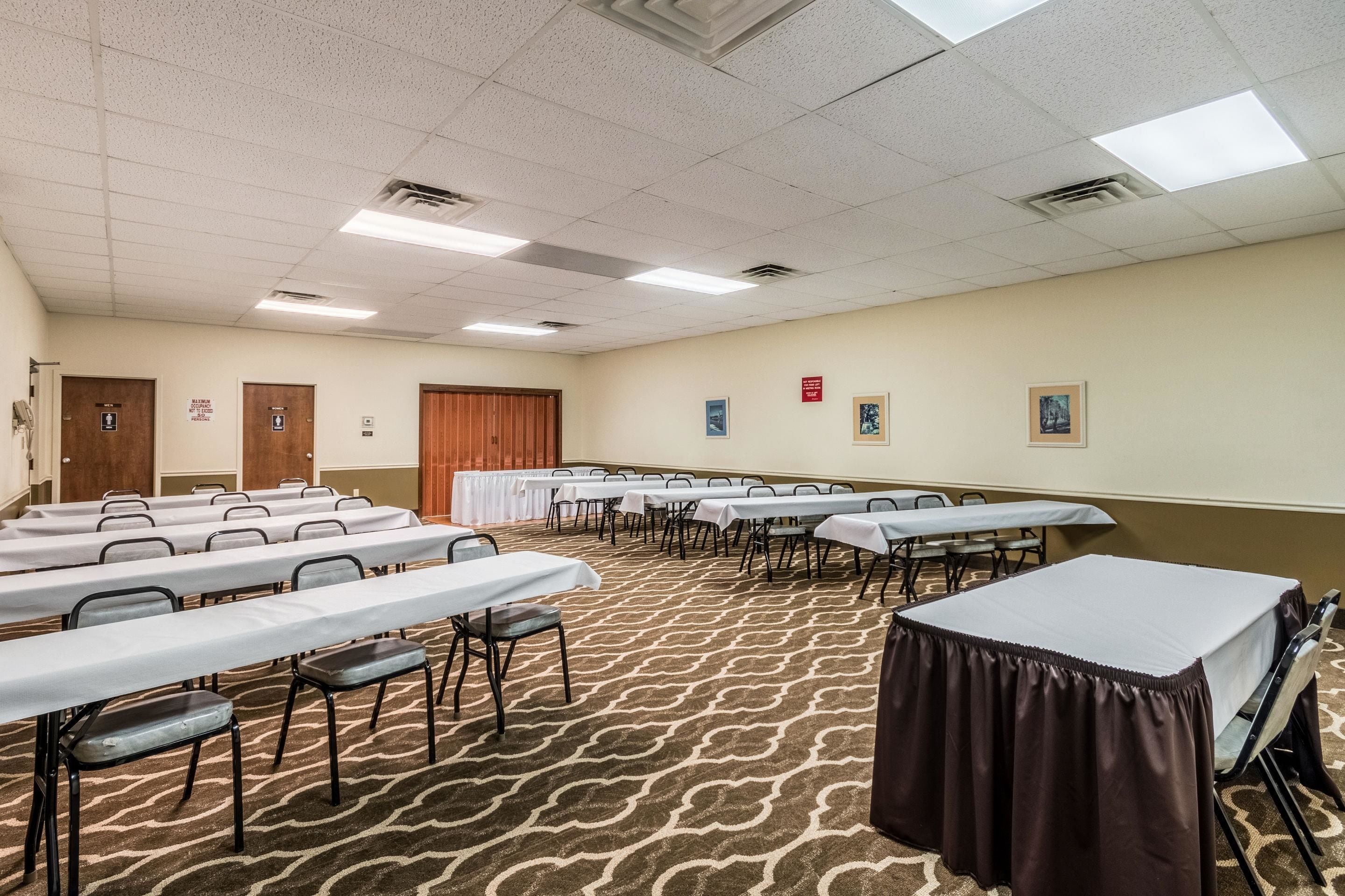 Une salle de conférence avec plusieurs tables et chaises, un sol recouvert de moquette et une porte au fond.