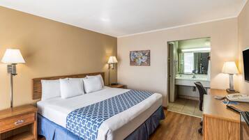 Une chambre d’hôtel avec un grand lit, des tables de chevet avec des lampes, un bureau avec une chaise et une salle de bain visible à travers une porte ouverte.