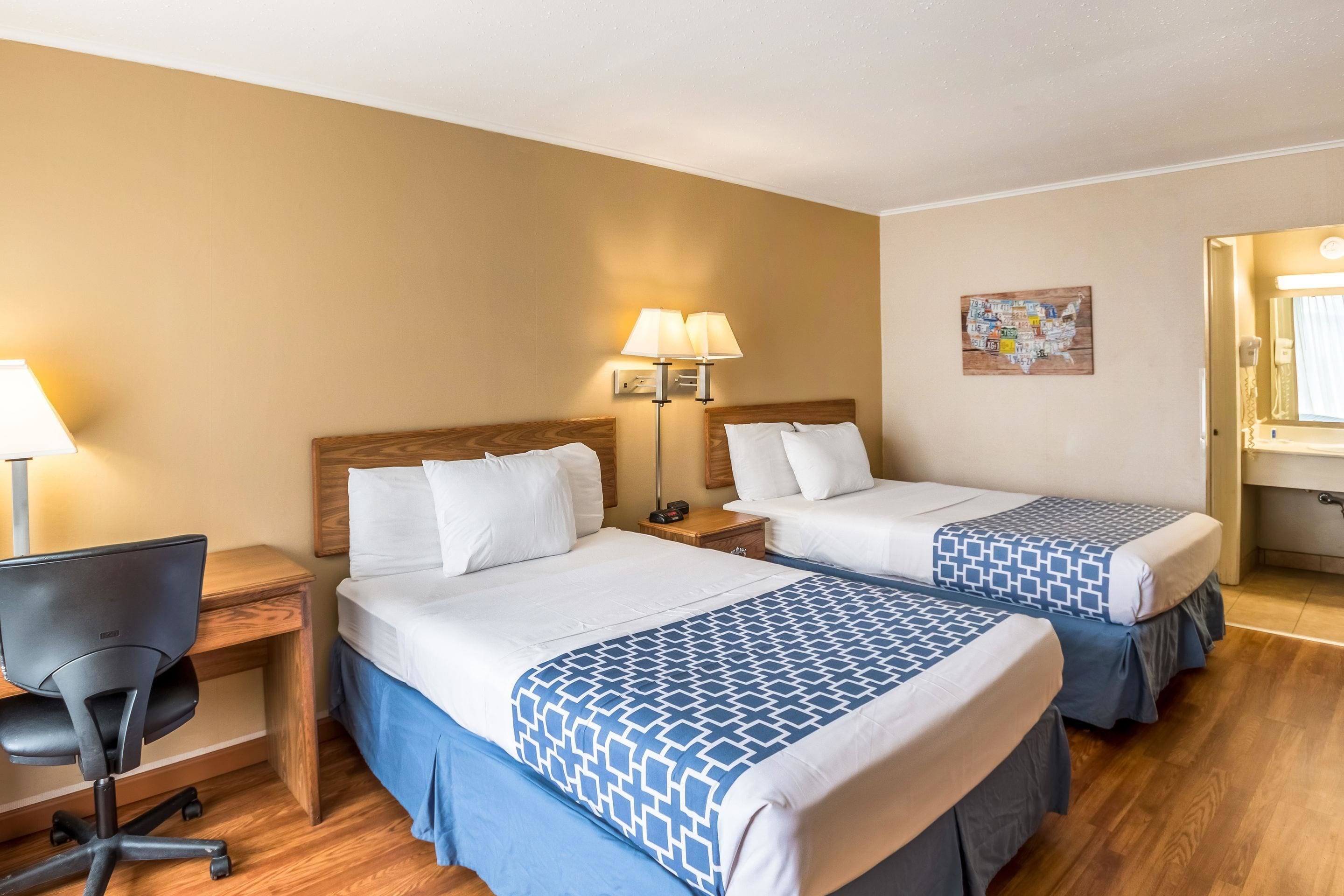 Una habitación de hotel con dos camas, un escritorio, una silla y una mesita de noche con lámparas.