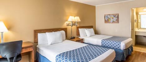 Una habitación de hotel con dos camas, un escritorio, una silla y una mesita de noche con lámparas.