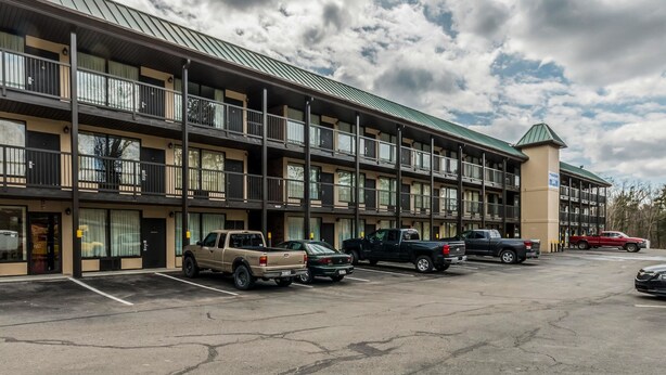 A multi-story motel with a green roof, parking lot, and several parked vehicles. - Smart Extended Stay (Beckley)