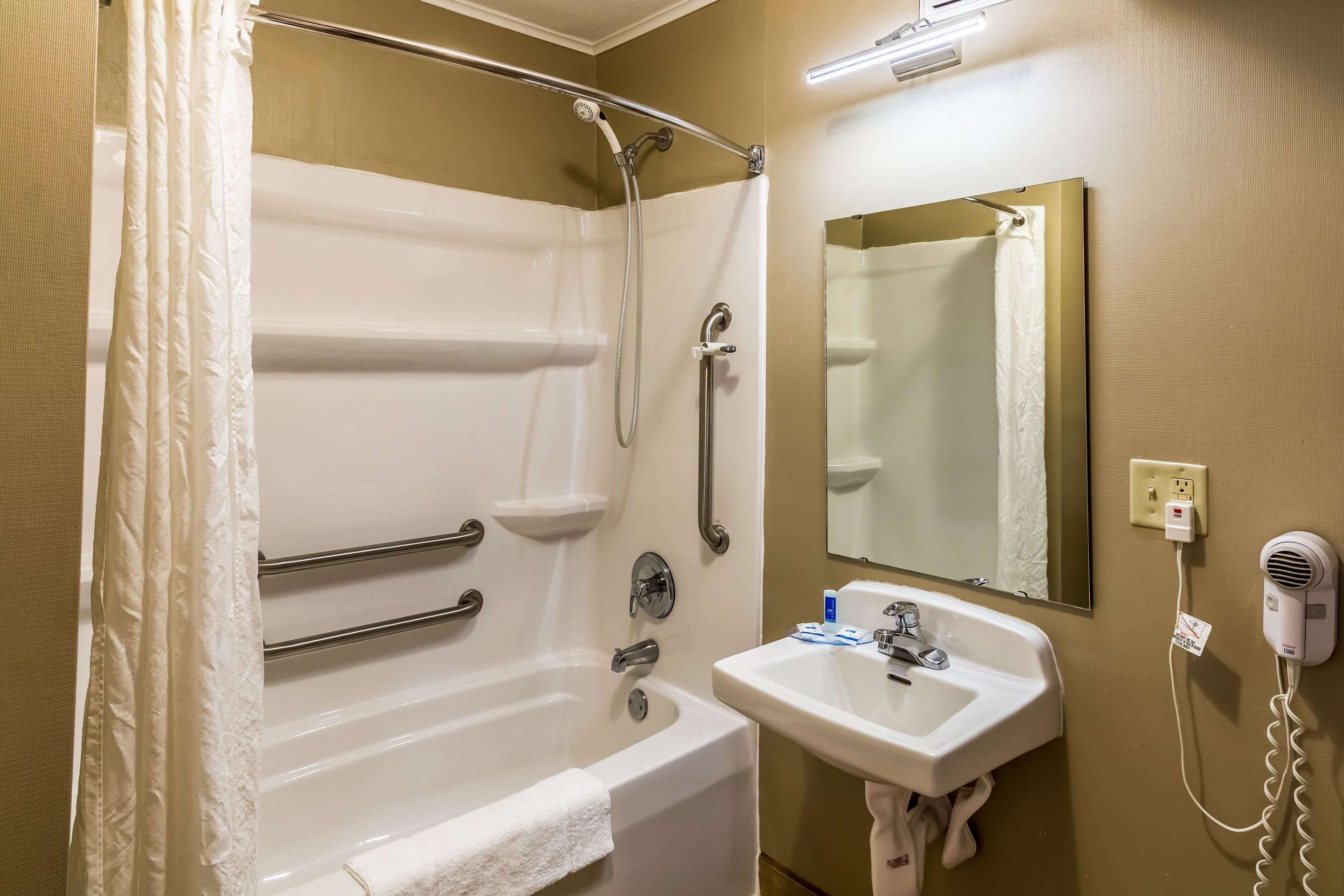 A bathroom with a bathtub, a hand dryer, a sink, and a mirror.