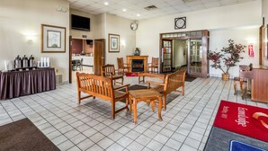 A hotel lobby with a tiled floor, wooden furniture, a fireplace, a television, and a red carpet with the hotel name. - Smart Extended Stay (Beckley)