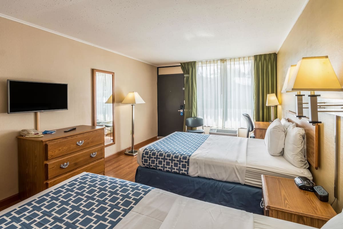 A hotel room with two beds, a TV, a desk, and a chair.