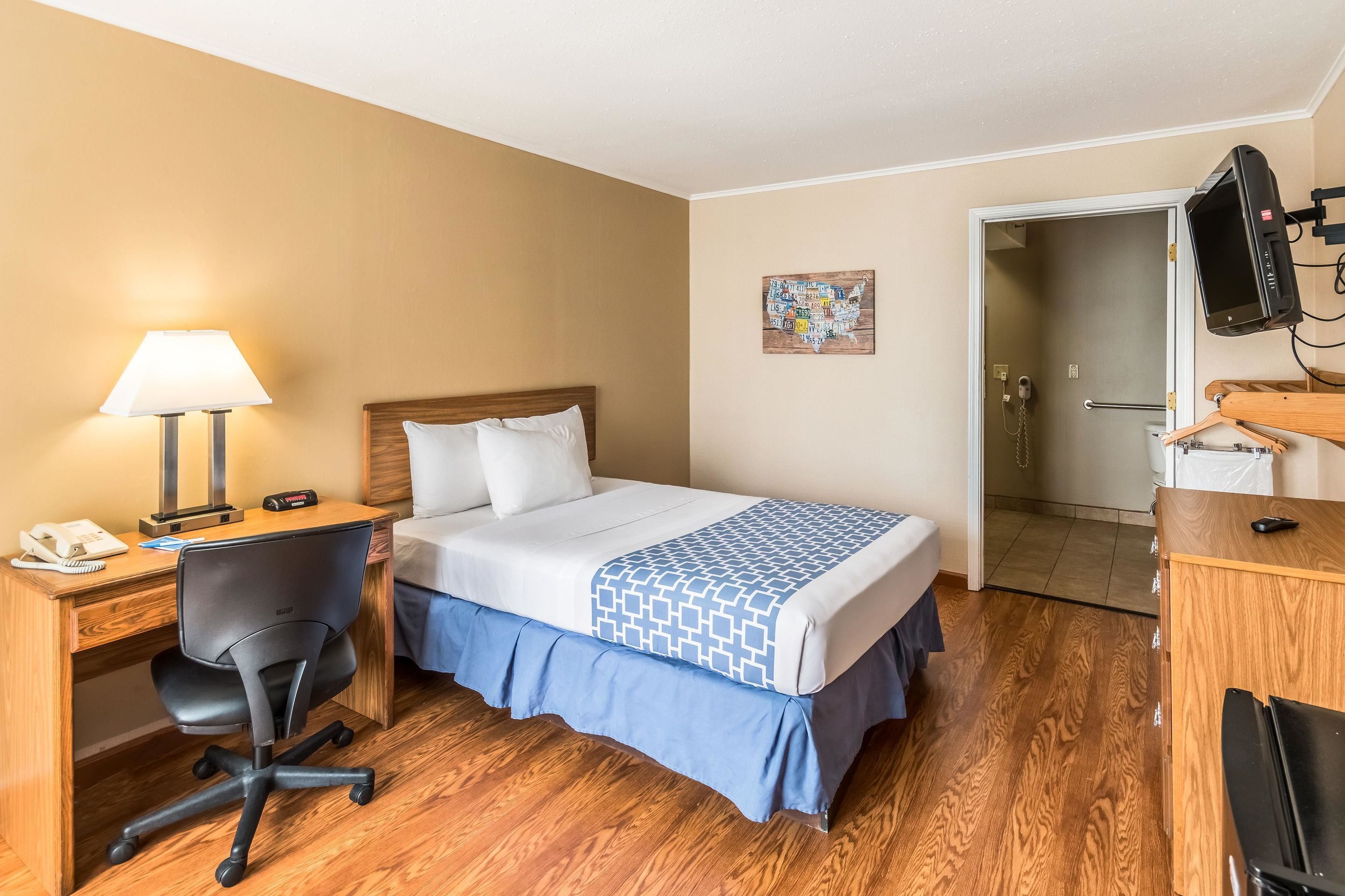 Une chambre d’hôtel équipée d’un lit, d’un bureau, d’une chaise et d’un téléviseur fixé au mur.