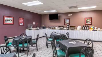 A dining area with tables and chairs, a buffet setup, and a television on the wall.