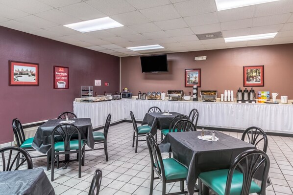 Un comedor con mesas y sillas, una barra de buffet y un televisor en la pared.