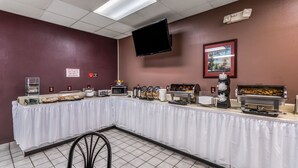 Montaje de bufé con una larga mesa cubierta con tela blanca, diferentes estaciones de comida, un microondas y un televisor de pantalla plana montado en la pared.