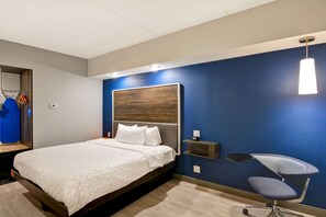 Una habitació d'hotel moderna amb un llit gran, un escriptori amb cadira, una prestatgeria penjada a la paret i una làmpada penjant.