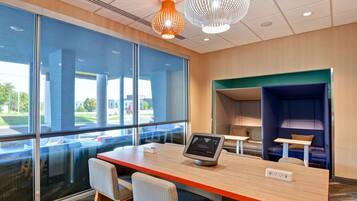 A modern office space with a large window, a desk with a computer, and a seating area with a blue booth.