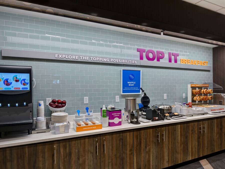 Mostrador de desayuno con un cartel que dice "TOP IT BREAKFAST" y una barca de gofres.
