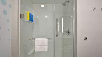 Doccia vetrata con asciugamano bianco su un porta asciugamani, porta doccia in vetro e dispenser per asciugamani a parete con flaconi.