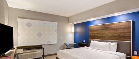 A modern hotel room with a large bed, a desk with a computer, a chair, and a TV.