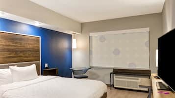 A modern hotel room with a large bed, a desk, a chair, and a TV.
