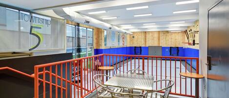 A modern indoor space with a glass wall displaying 'Township 5', a basketball court with a red railing, and a table with chairs.