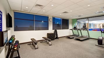 Une salle de sport équipée de tapis de course, de bancs de musculation et de kettlebells.