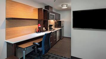A modern kitchen with a built-in microwave, refrigerator, and a large flat-screen TV mounted on the wall.