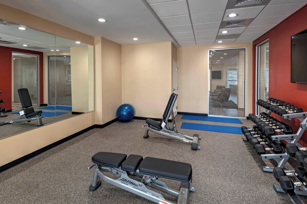 A gym with exercise equipment, a mirrored wall, and a blue mat on the floor.