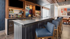Uma área de bar moderna com um balcão comprido, banquetas e uma variedade de garrafas e copos.