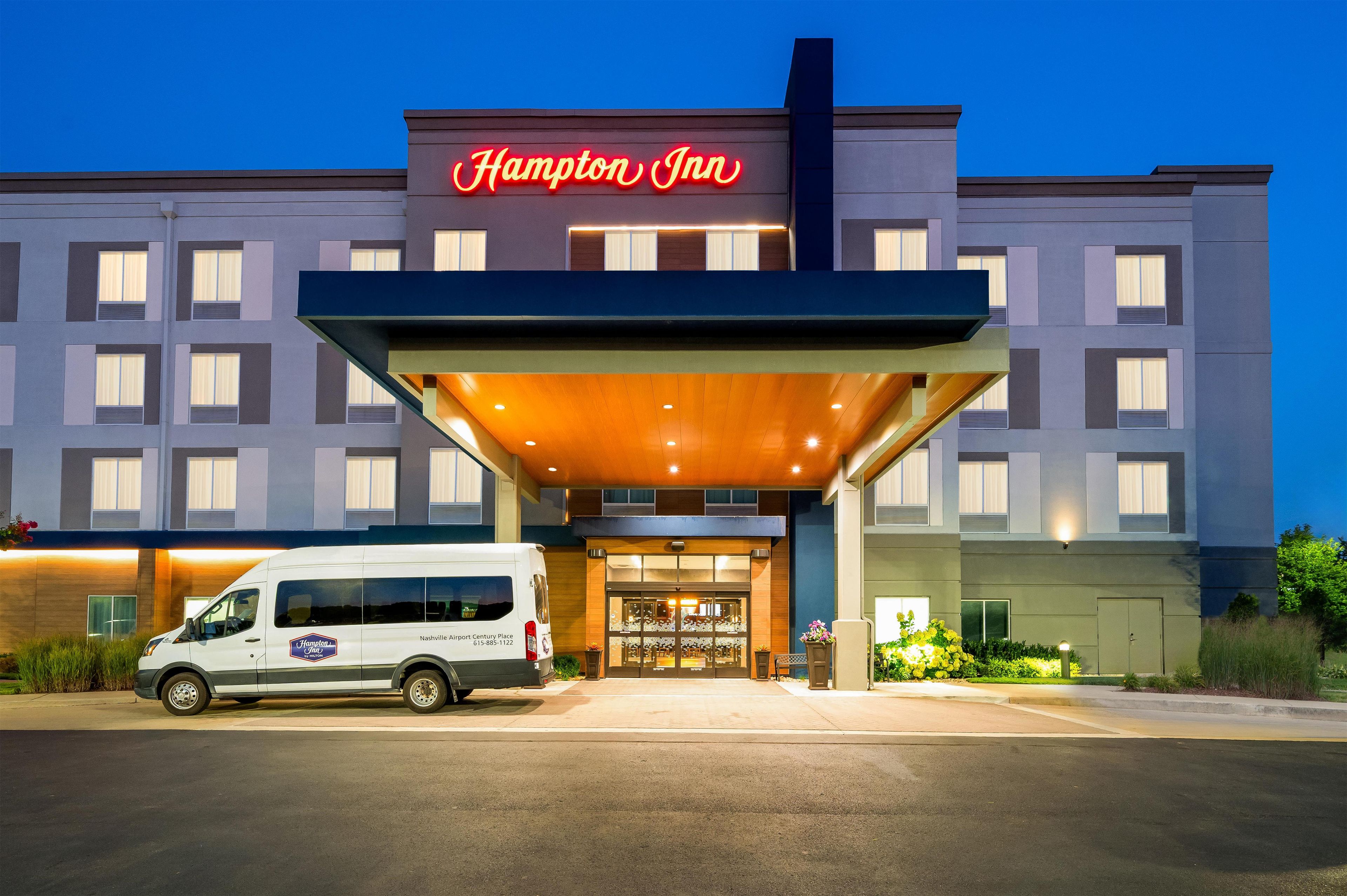 Un hotel Hampton Inn con una fachada moderna, una entrada cubierta y una furgoneta estacionada en frente.