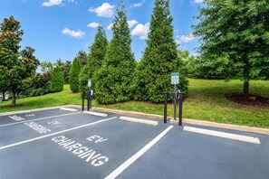 Un área de estacionamiento con estaciones de carga para vehículos eléctricos, espacios de estacionamiento delimitados y un letrero verde que indica la ubicación de la estación de carga.