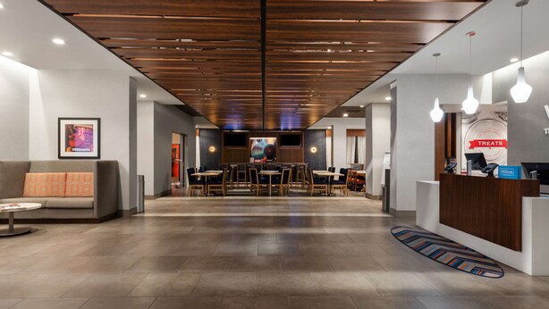 Um hall de hotel com design moderno, com balcão de recepção, área de estar e uma tela grande.