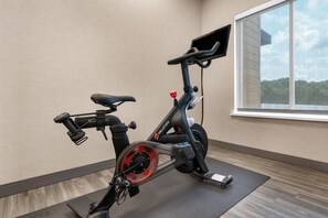 Una bicicleta estática en una habitación con ventana, suelo de madera y una estantería en la pared.
