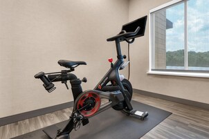 An exercise bike in a room with a window, a wooden floor, and a wall-mounted shelf.