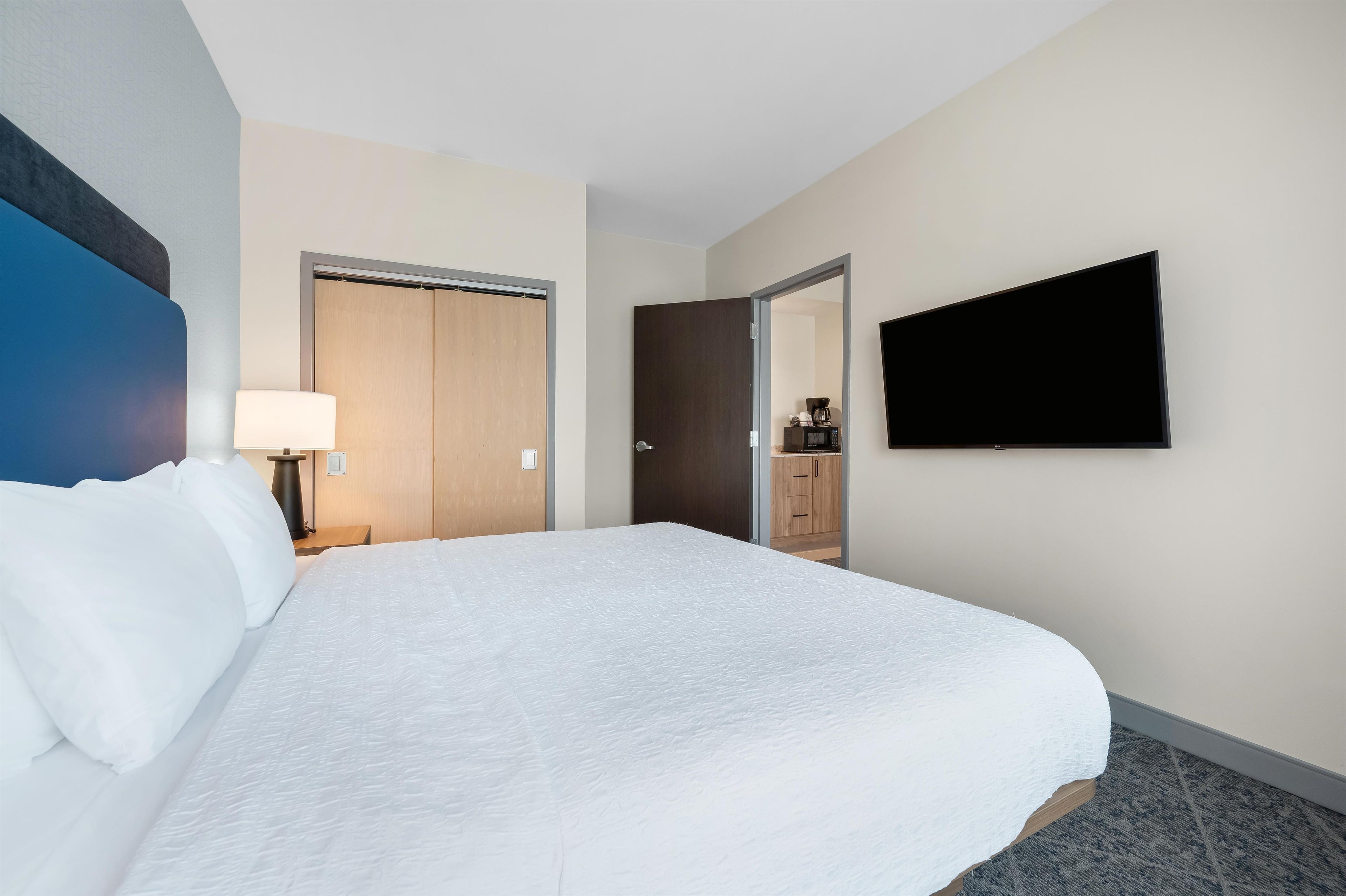 Una habitación de hotel con una cama grande, un televisor de pantalla plana, un armario y una pequeña kitchenette.