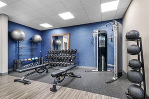 Academia com equipamentos de ginástica, incluindo um banco, halteres e suporte para agachamento.