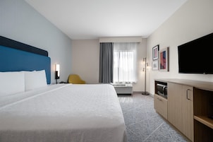 Ein Hotelzimmer mit einem großen Bett, einem Schreibtisch, einem Sessel, einem Flachbildfernseher und einer Minibar.