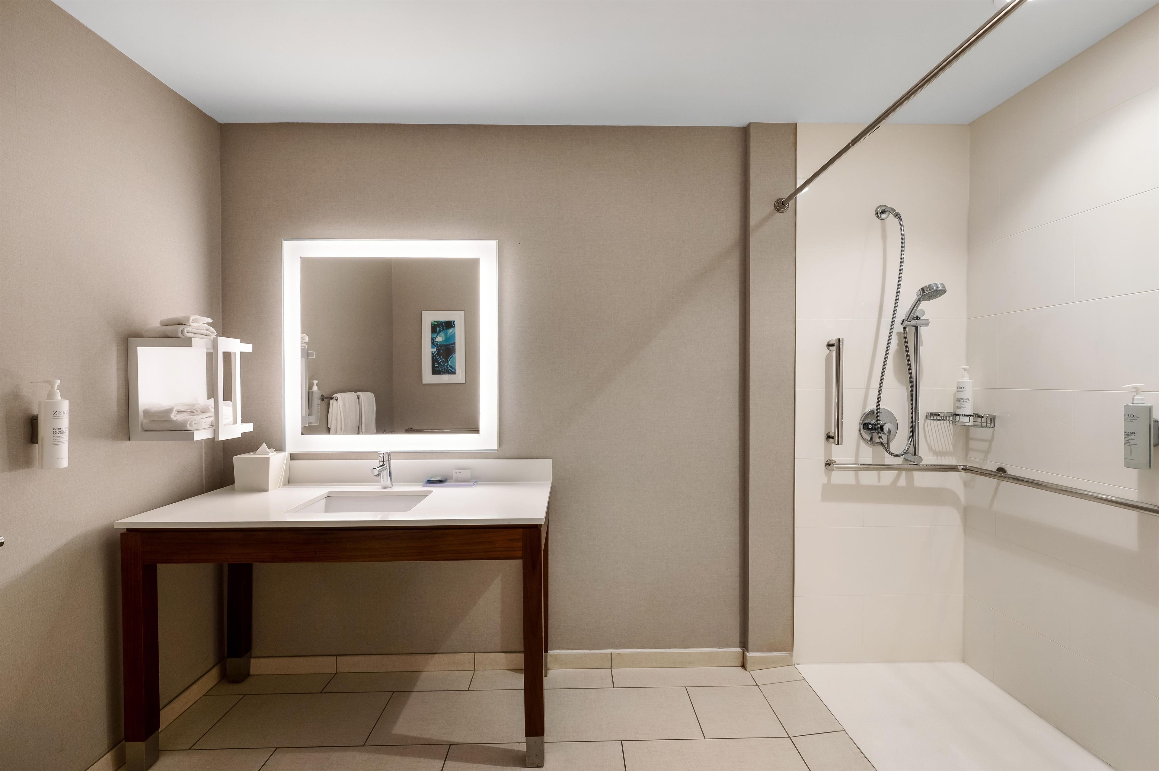 A modern bathroom with a white vanity, a large mirror, a shower area with a handheld showerhead, and a towel rack.