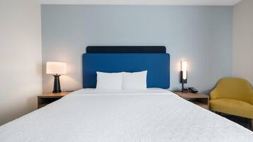 A hotel room with a bed, two bedside tables, a lamp, a phone, and a chair.