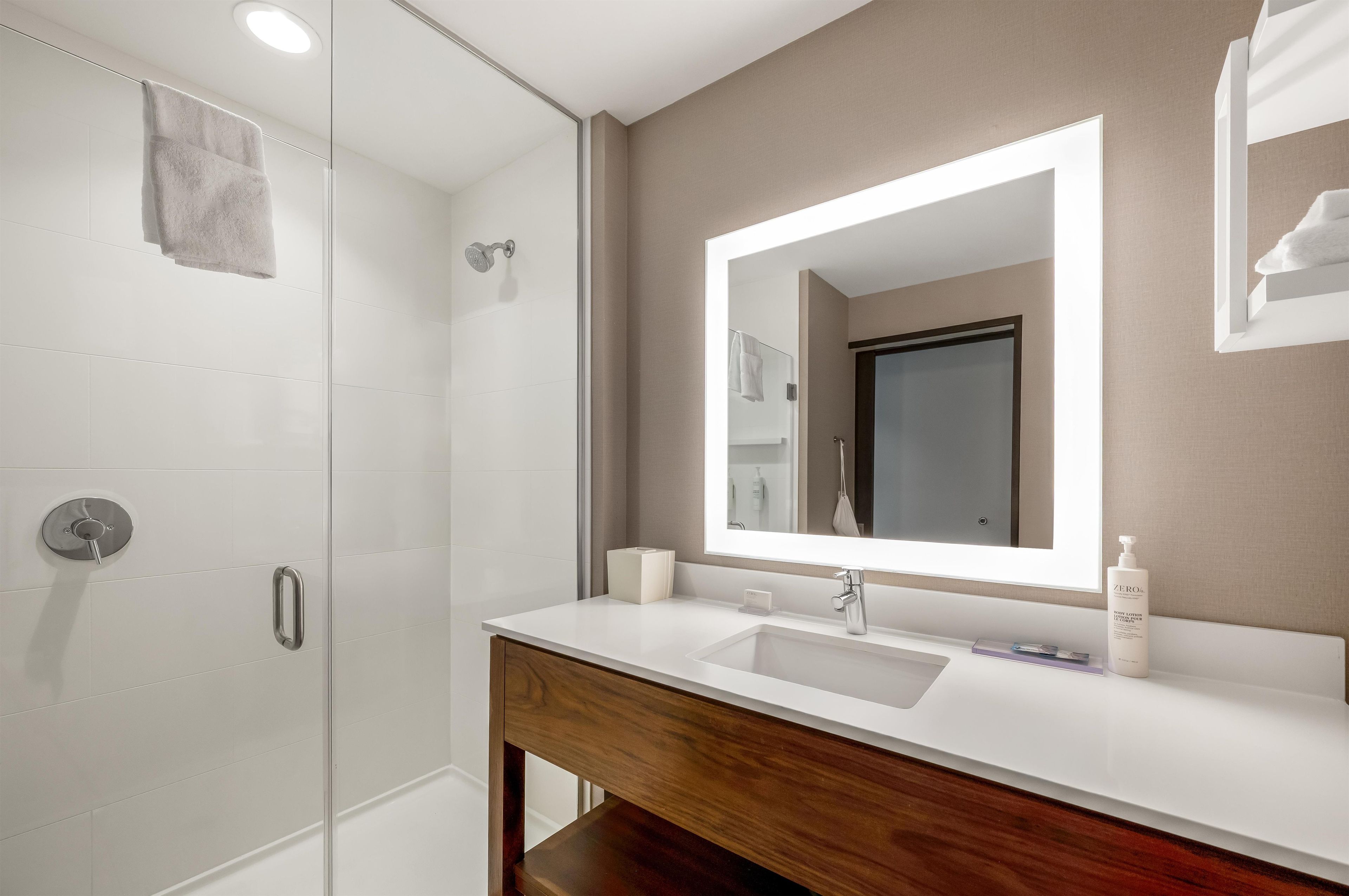 A modern bathroom with a glass shower enclosure, a wooden vanity, and a large mirror.
