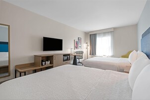A hotel room with two beds, a TV, a desk with a microwave, and a chair.