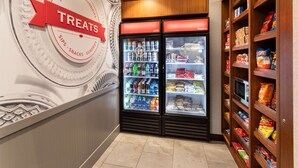 Exposição de guloseimas refrigeradas com um letreiro 'TREATS', prateleiras repletas de lanches e uma parede com um padrão circular decorativo.