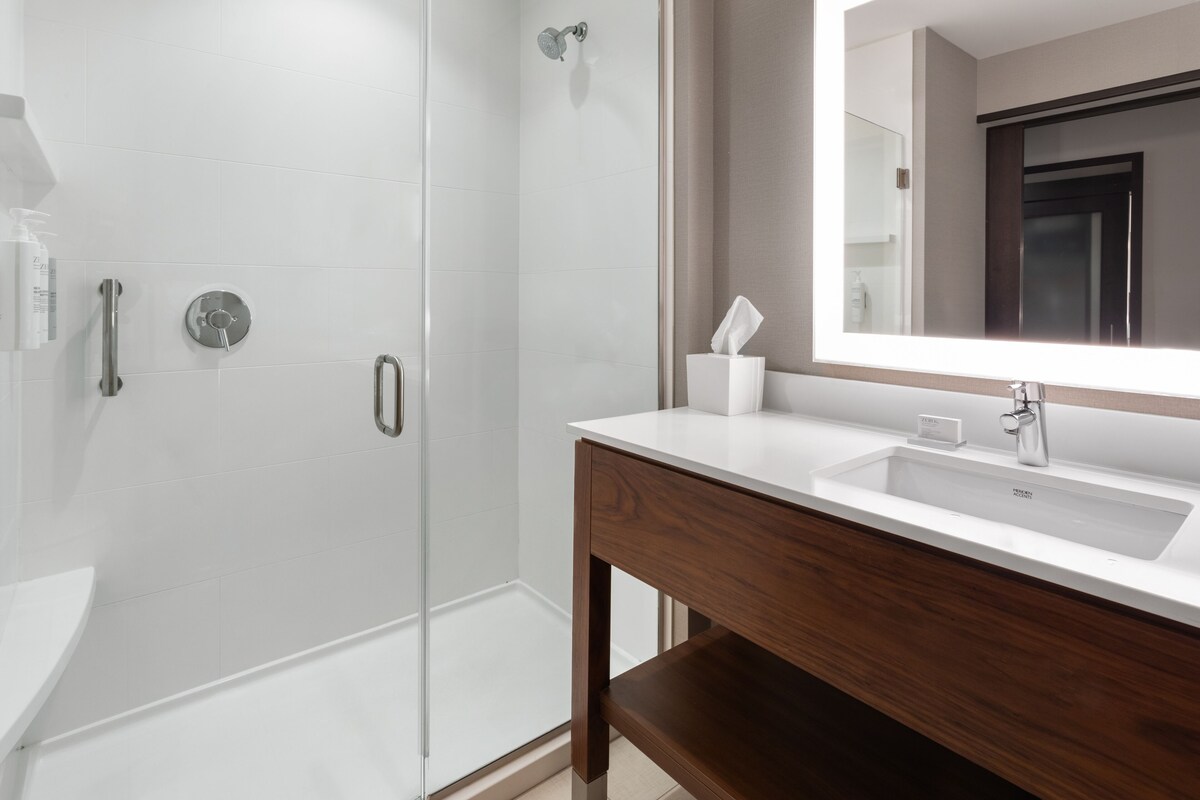 A modern bathroom with a glass shower enclosure, a white sink with a wooden vanity, and a large mirror above the vanity.