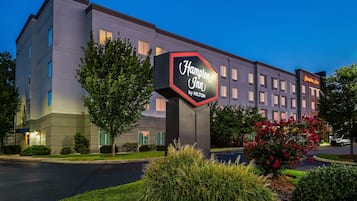 Een Hampton Inn by Hilton hotel met een groot bord, meerdere ramen en verzorgde beplanting.