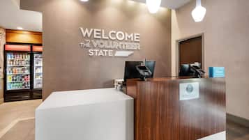 A reception desk with a 'WELCOME THE VOLUNTEER STATE' sign, a minibar, and a 'Hilton Honors' loyalty program sign.