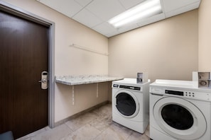 A laundry room with a door, a countertop, and two washing machines. - Hampton Inn Nashville Airport Century Place, TN (Nashville)