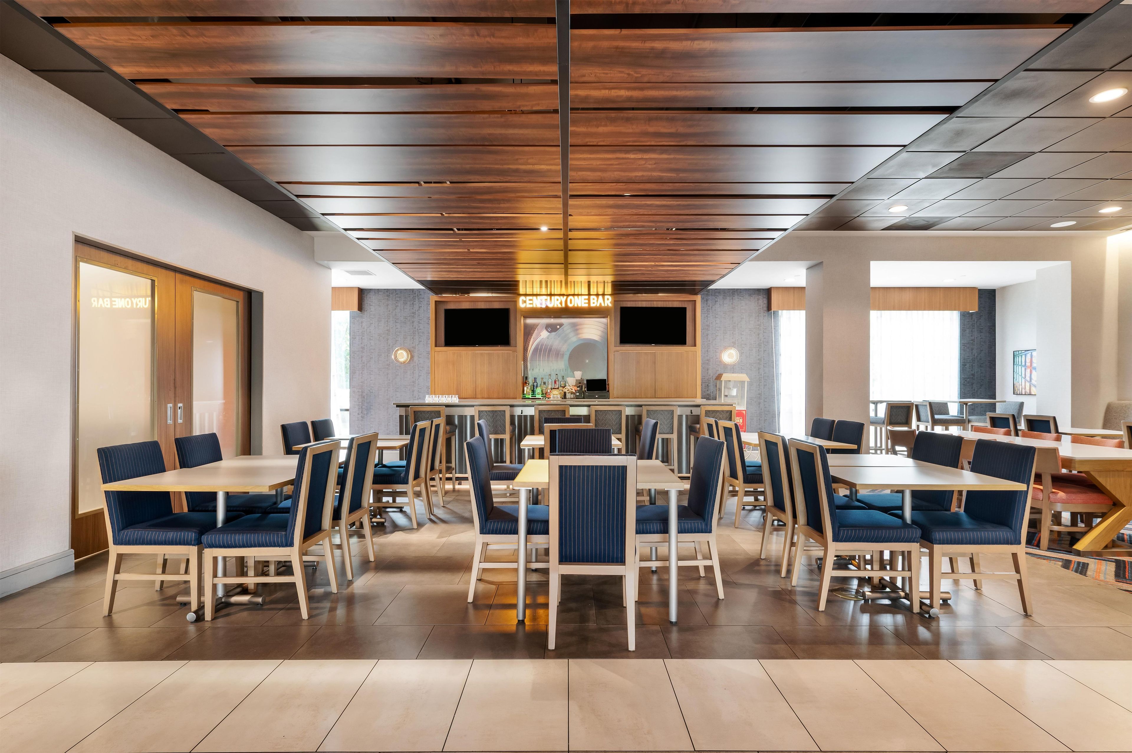 A modern dining area with multiple tables and chairs, a bar area, and a television screen.