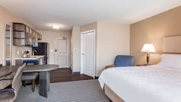 A hotel room with a bed, a desk with a chair, a lamp, and a door leading to a bathroom.