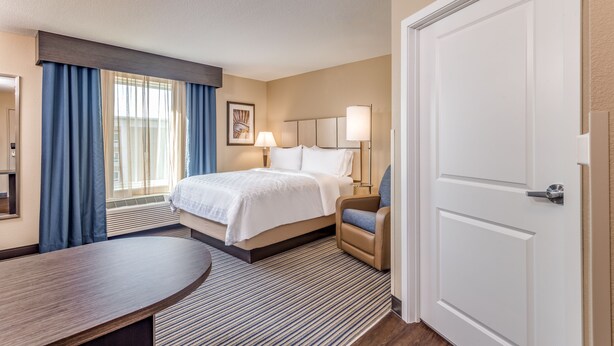 A hotel room with a bed, a desk, a chair, a lamp, and a door. - Candlewood Suites Eau Claire I-94 by IHG (Eau Claire)