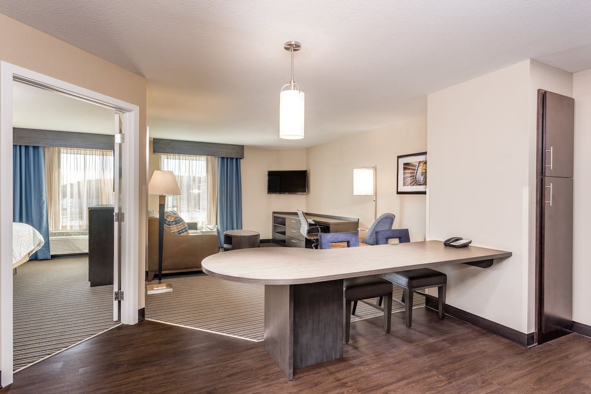 A modern hotel room with a large desk, a flat-screen TV, a refrigerator, and a bed with curtains.